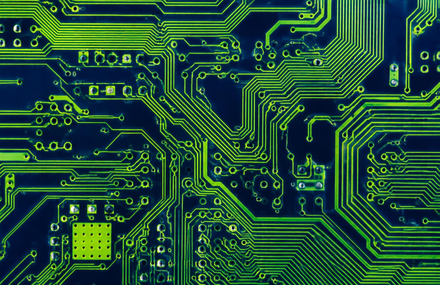Macro photograph of a circuit board with bright green traces over a navy substrate